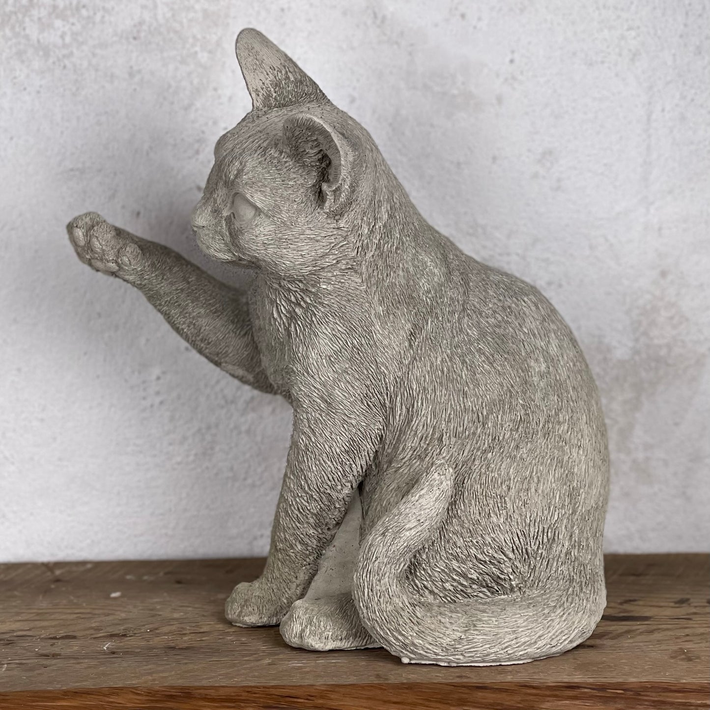 Detaljerad betongfigur av busig sittande katt med uppsträckt tass