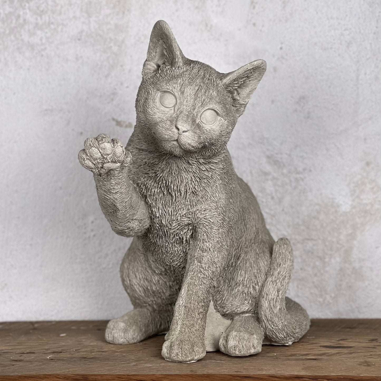 Betongkatt Ture som sitter och lyfter tassen i busig hälsning