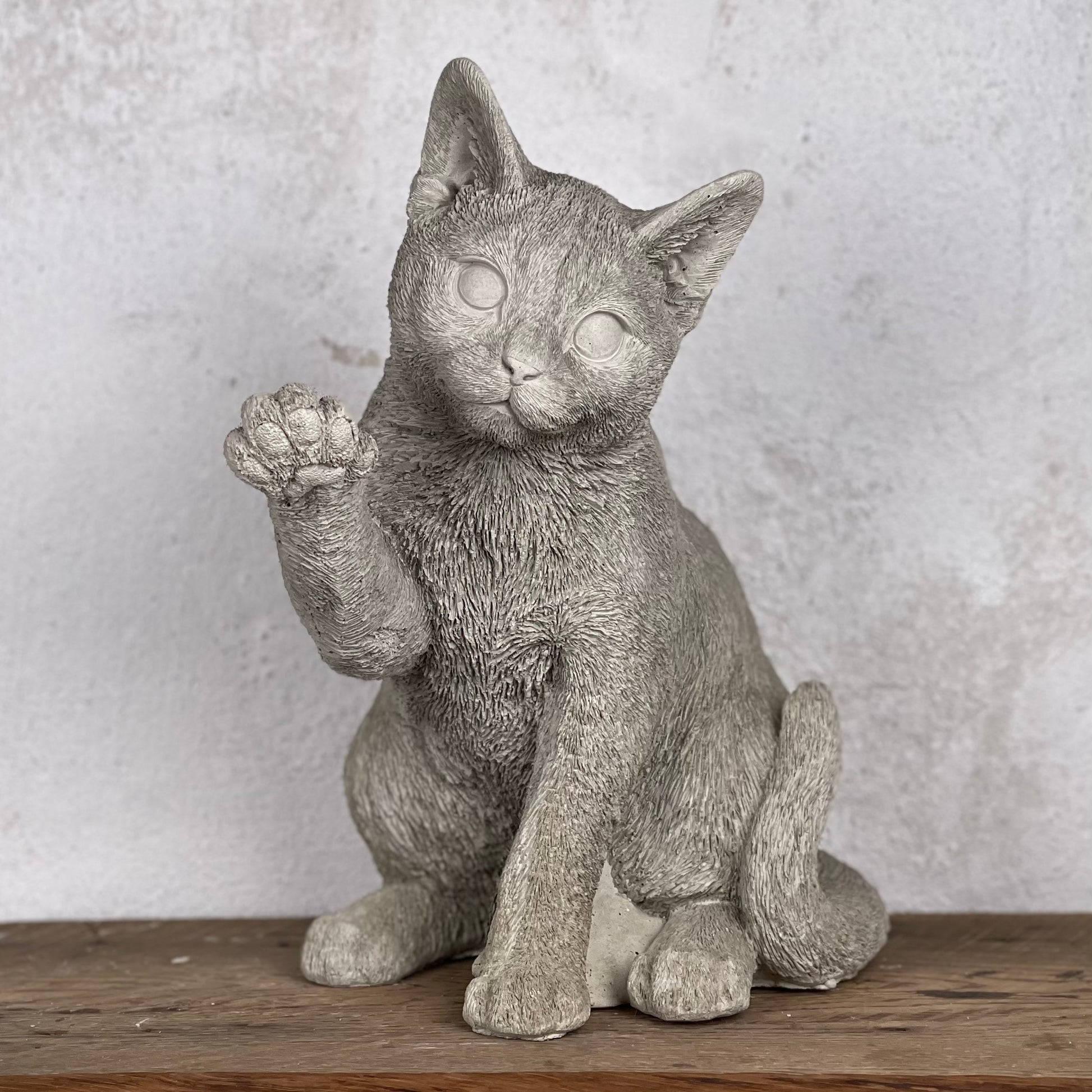 Betongkatt Ture som sitter och lyfter tassen i busig hälsning