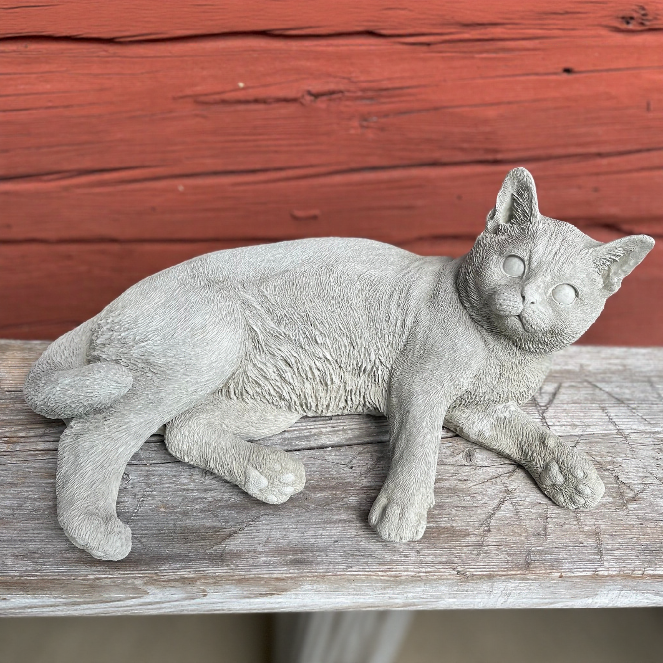 Betongfigur av liggande katt, Daisy, som lyfter huvudet och tittar upp